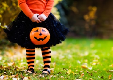 Enfant en costume d’Halloween tenant un seau à bonbons en forme de citrouille dehors.